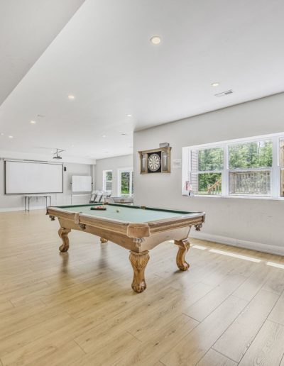 Recreational room with pool table, dartboard, wooden floor, projector screen, and office chair.