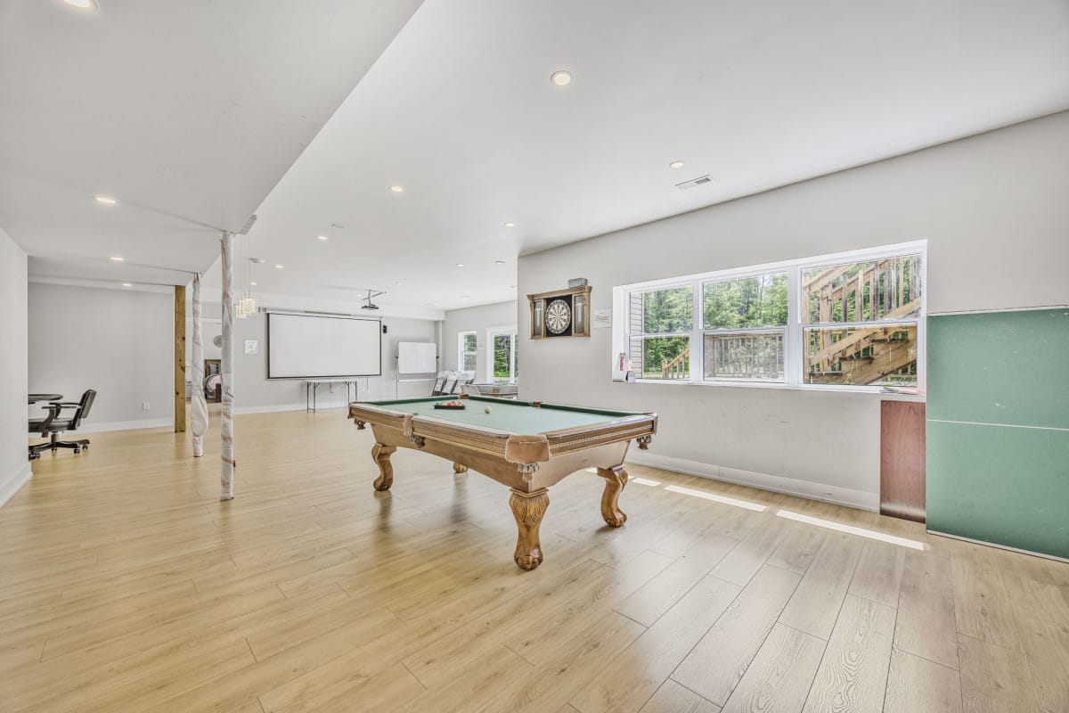 Recreational room with pool table, dartboard, wooden floor, projector screen, and office chair.