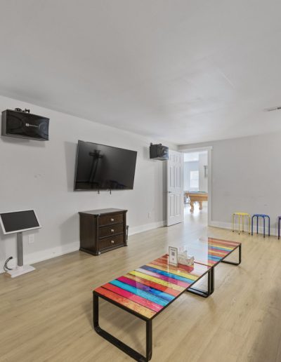 Living room with brown leather sofa, colorful striped table, TV, speakers, and light wood floor.