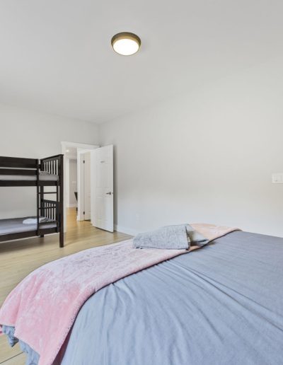 Bedroom with a large bed, dark wooden bunk beds, light flooring, and open bathroom door with toilet.