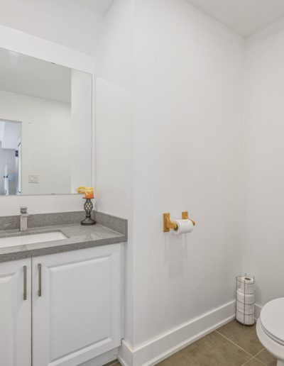 Minimalist bathroom with white toilet, white vanity, gray countertop, mirror, and toilet paper holder.