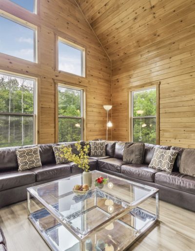Living room with wood-paneled walls, large leather sectional sofa, glass coffee table, and dining area.