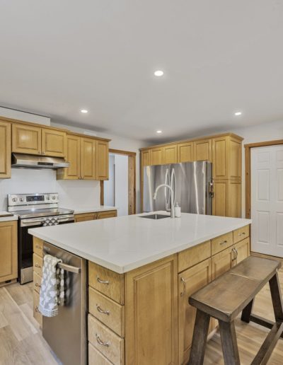 Modern kitchen with light wood cabinets, central island with sink, stainless appliances, and bench.
