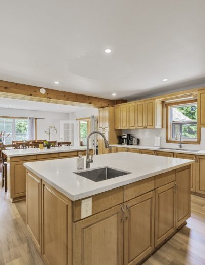 Spacious kitchen with wooden cabinets, two islands with sinks, dining area, and large windows.