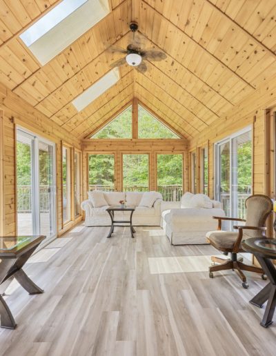 Sunroom with wooden walls and ceiling, light wood flooring, white sofas, chairs, and glass tables.
