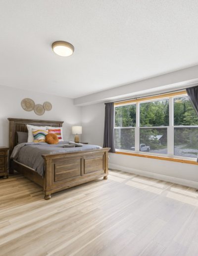 Bedroom with wooden bed, gray bedding, nightstands with lamps, large window, and light wood floor.