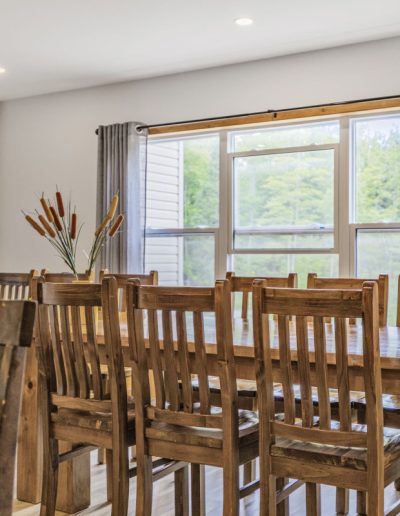Long wooden dining table with multiple chairs near large windows with gray curtains.