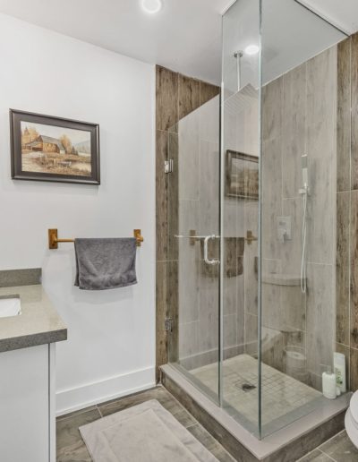 Bathroom with glass shower, wood-textured tile walls, white toilet, gray countertop, and gray towel.