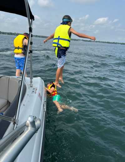 Children wearing life jackets swimming and jumping from a boat on a partly cloudy day.