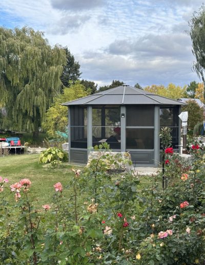 Garden with blooming roses, central screened gazebo, large trees, dock with canoes, and lounge chairs.