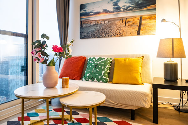 Living room with wooden walls, large windows, dark leather sectional sofa, and glass coffee table.